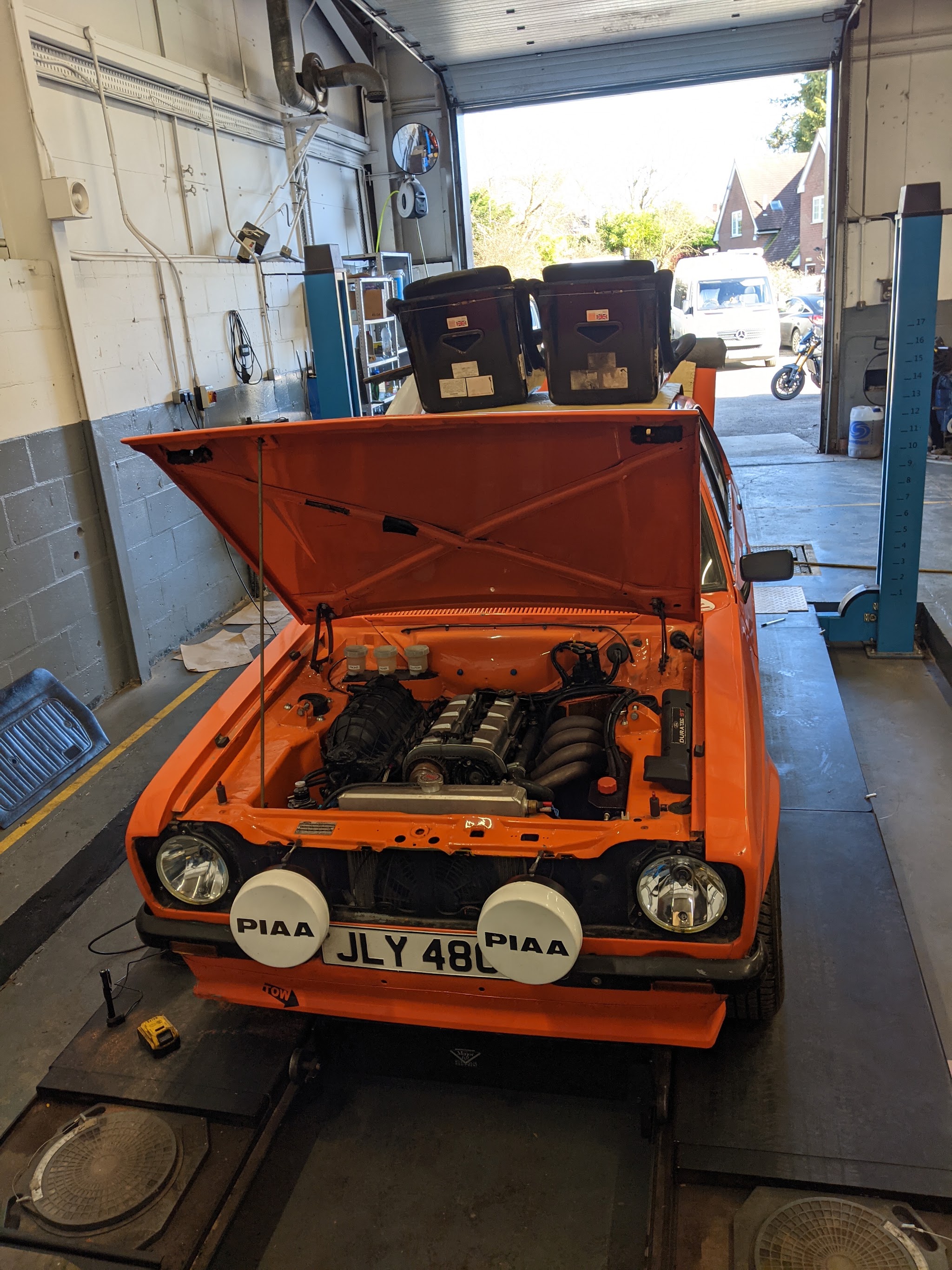 An orange classic Ford Escort with its bonnet up on the ramp at Morris Autos